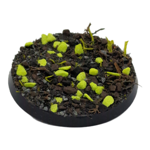 Round miniature base with dark brown texture and bright green sprouts on a white background