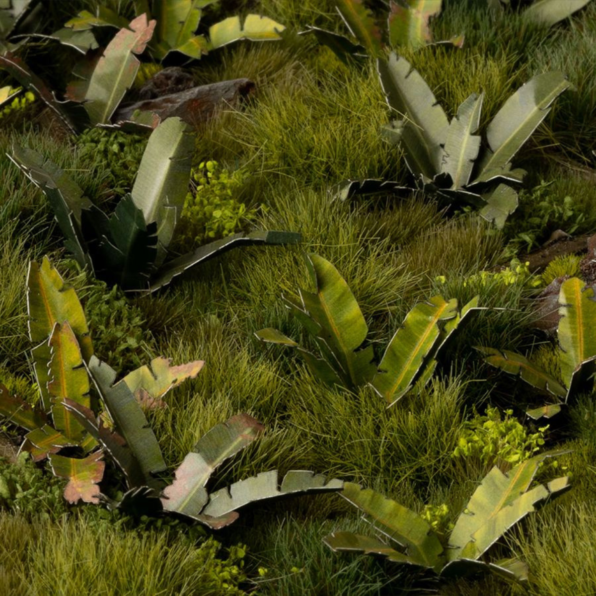 A close-up view of a textured faux grass and foliage landscape, featuring green and yellow-green grass blades interspersed with tropical-style leaves in various shades of green.