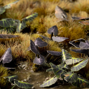 A close-up of artificial decorative butterflies with dark purple-black wings and bright yellow-green veining, arranged among tan grass-like material and a small pool of water.