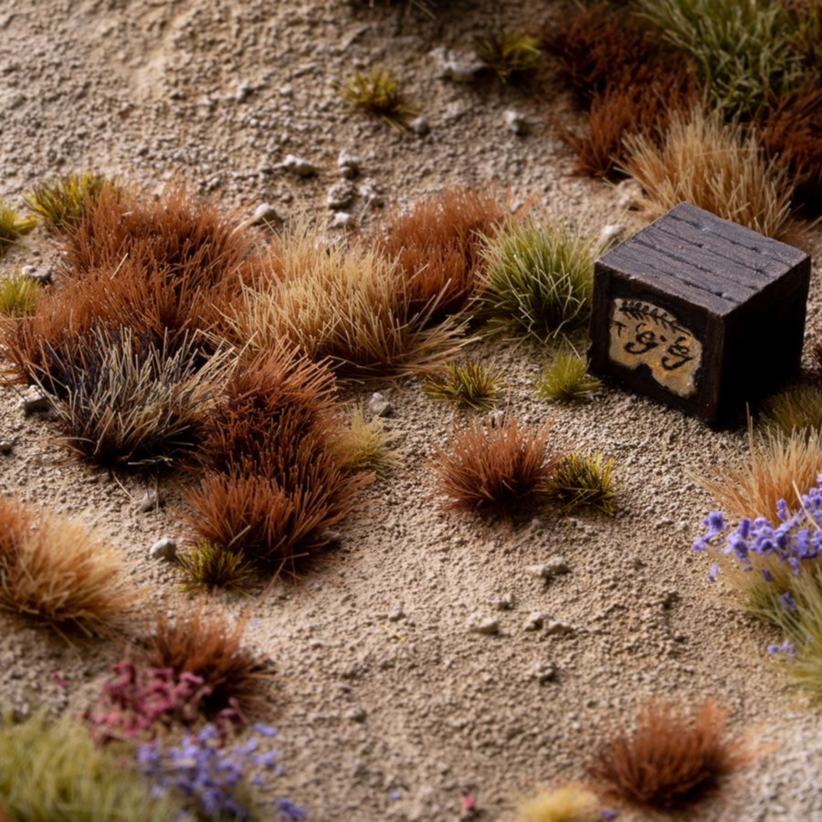 Small wooden block with text on a sandy surface with grass and flowers