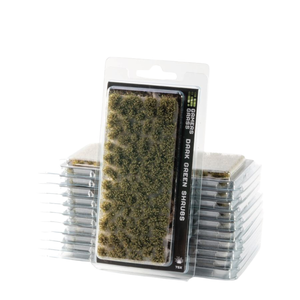 Packaged miniature grass shreds in dark green, shown in a clear blister pack with a stack of similar packs behind it on a white background.