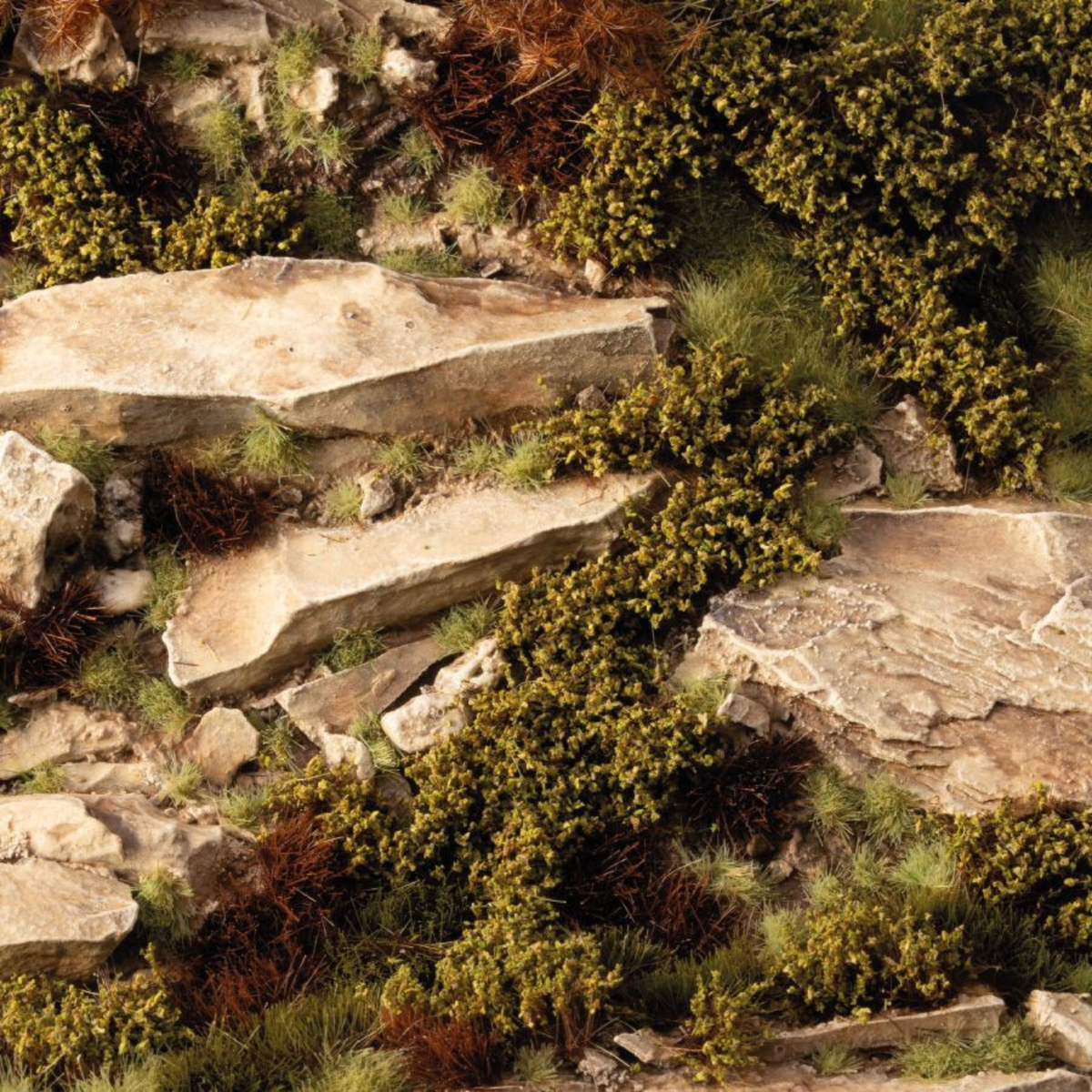 A close-up of a textured surface featuring natural-looking beige rocks, green and brown low-lying plants, and small tufts of grass, resembling a stone wall or forest floor texture.