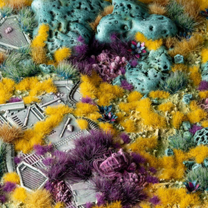A highly detailed, colorful miniature terrain setup featuring textured gray roads, small buildings, and various artificial plants in vibrant yellow, purple, and teal-green.