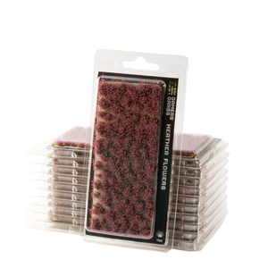 Packaged heathered flowers mini terrain pieces by TPK, featuring a clear blister pack with a black label displaying the textured purple and pink heathered surface, with stacks of individual packaged pieces behind it on a white background.