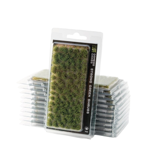 Packaged miniature green shrubs for tabletop wargaming, with one clear blister pack standing in front of stacked sheets of the same product on a white background.