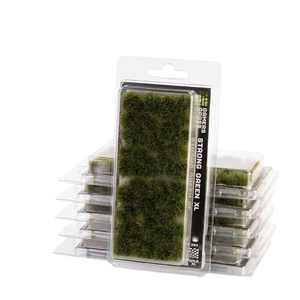 Packaged green artificial moss or turf pieces in clear plastic blister packaging, with one package standing upright in front of several stacked packages on a white background.