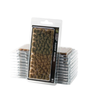 Packaged miniature terrain piece labeled 'SWAMP SHRUBS' in a clear blister pack, with several additional packs stacked behind it on a white background.